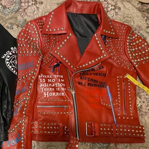 May include: Red leather jacket with silver studs and a black zipper. The jacket has several phrases written on it, including "Where there is no imagination there is no horror" and "Life is not a sound the music rings is a lifestyle".