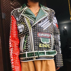 May include: A black leather jacket with a green collar and white trim. The jacket is covered in silver studs and has various patches with text including "Fear", "Varukers", "The Exploited", and "Drillers".