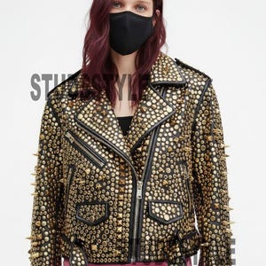 Può includere: Giacca in pelle nera e oro borchiata con chiusura a zip e cintura. La giacca è ricoperta di borchie e punte dorate. La parola "STYLE" è visibile sulla giacca.