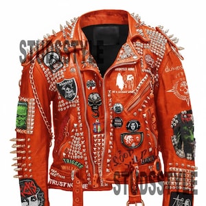 May include: Bright orange leather jacket adorned with silver studs and spikes. The jacket is decorated with patches featuring skulls and graphic designs, plus the text "TRIGGER" and "TRUST NO ONE". A belt with a buckle is present.