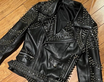 May include: Black leather jacket with silver studs and a belt. The jacket has a zipper closure and a pointed collar.