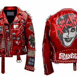 Puede incluir: Chaqueta de cuero roja adornada con numerosos tachuelas y parches met&aacute;licos. La chaqueta presenta una variedad de dise&ntilde;os, incluyendo calaveras, personajes de dibujos animados y texto. La parte trasera de la chaqueta muestra un gr&aacute;fico de una cara sonriente y la palabra "PUNKS!!".