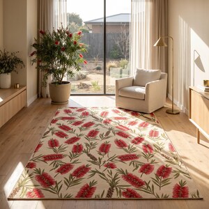 Puede incluir: Una alfombra rectangular con un patrón botánico repetitivo de flores rojas de limpiatubos y hojas verdes sobre un fondo color crema. La alfombra está colocada sobre un suelo de madera clara en una habitación con un gran ventanal y una planta.