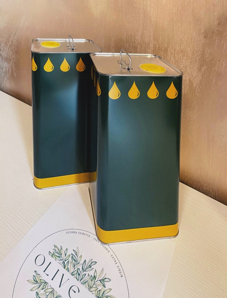 May include: Two green metal olive oil cans with yellow lids and yellow oil drop designs. The cans are sitting on a white surface with a circular logo that says "OLIVE" in green.