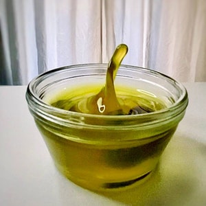 May include: A clear glass bowl filled with a yellow liquid. The liquid is rippling and has a single, tall, pointed wave in the center.