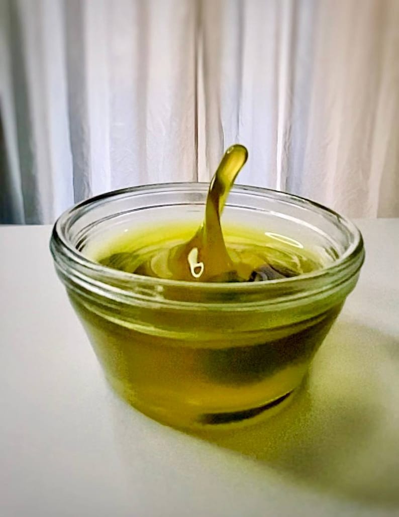 May include: A clear glass bowl filled with a yellow liquid. The liquid is rippling and has a single, tall, pointed wave in the center.