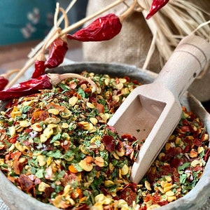 Peut inclure: Une cuillère en bois remplie d'un mélange d'herbes séchées, d'épices et de flocons de piment rouge. Le mélange est un mélange vibrant de vert, de rouge et de jaune.
