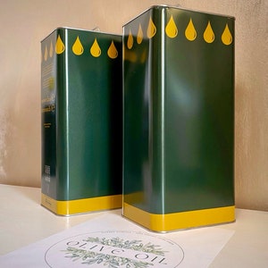 May include: Two green metal olive oil containers with yellow lids and yellow olive drop designs. The containers are sitting on a white surface with a circle logo that says "Olive Oil" in green lettering.