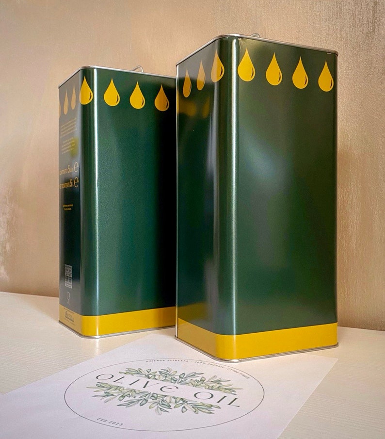May include: Two green metal olive oil containers with yellow lids and yellow olive drop designs. The containers are sitting on a white surface with a circle logo that says "Olive Oil" in green lettering.