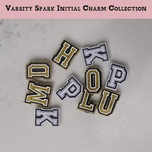 Puede incluir: Colección de dijes iniciales Varsity Spark. Dije iniciales en oro, negro y blanco. Los dijes son de estilo universitario, con un borde dorado brillante. Las letras incluyen D, H, K, M, O, P y U.