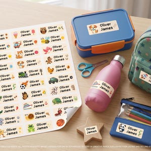 May include: A sheet of rectangular adhesive labels featuring the name Oliver James alongside various colourful cartoon illustrations of animals, vehicles, and sports items. Similar personalised stickers are applied to a blue lunch box, a pink water bottle, a star-shaped wooden block, a green star-patterned backpack, and a blue pencil case.