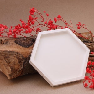 Könnte beinhalten: Weiße sechseckige Keramik-Schale mit glatter Oberfläche. Die Schale liegt auf einem Stück verwittertem Holz mit roten Blumen auf beiden Seiten.