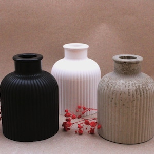 Könnte beinhalten: Drei Keramikvasen mit geripptem Design. Die Vasen sind schwarz, weiß und grau.