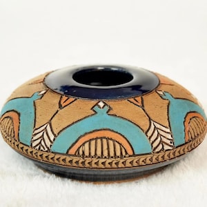 Peut inclure: Un bol en céramique fait à la main avec un intérieur bleu foncé et un extérieur beige. L'extérieur présente des motifs géométriques turquoise, orange et blancs. Le bol mesure environ 15 cm de diamètre et est une pièce décorative.