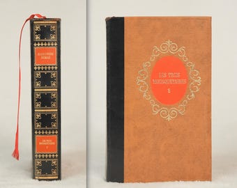 Op de afbeelding: Twee antieke boeken. Eén heeft een zwarte rug met gouden details en de naam van de auteur, Alexandre Dumas, is zichtbaar. De andere is bruin met de titel "Les Trois Mousquetaires" in gouden letters op een rode cirkel.