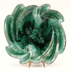 May include: A decorative, swirling green and black ceramic dish with a scalloped edge. The dish is supported by a gold-coloured metal stand. The interior features a marbled pattern of dark green and black.