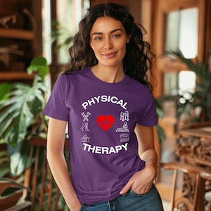 Op de afbeelding: Paars T-shirt met een wit cirkelvormig ontwerp met de tekst "PHYSICAL THERAPY" met een rood hart in het midden en witte pictogrammen van fysiotherapie-apparatuur rond het hart.