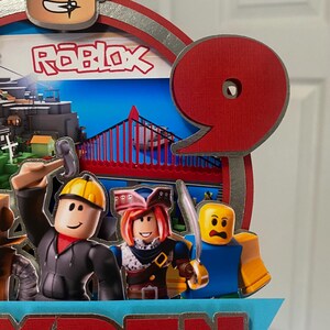May include: A red and silver Roblox themed cake topper with a number 9, a Roblox character, and the name "RYDEN".