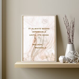May include: A framed print with a quote by Nelson Mandela on a white background with a subtle brown and gray marbled design. The quote reads "It always seems impossible until it's done."