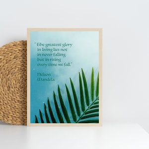 May include: A framed inspirational quote by Nelson Mandela on a blue background with a green palm leaf in the corner. The quote reads "The greatest glory in living lies not in never falling, but in rising every time we fall."