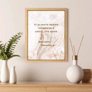 May include: A framed print with a quote by Nelson Mandela: "It always seems impossible until it's done." The background is a soft, abstract design in shades of beige and brown.