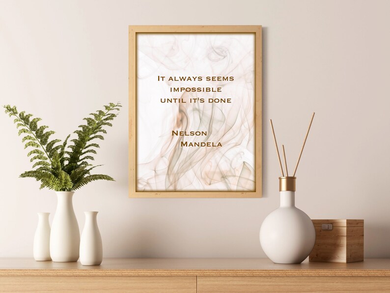 May include: A framed print with a quote by Nelson Mandela: "It always seems impossible until it's done." The background is a soft, abstract design in shades of beige and brown.