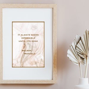 May include: A framed print with a quote by Nelson Mandela: "It always seems impossible until it's done." The background is a soft, abstract design in shades of pink and white.
