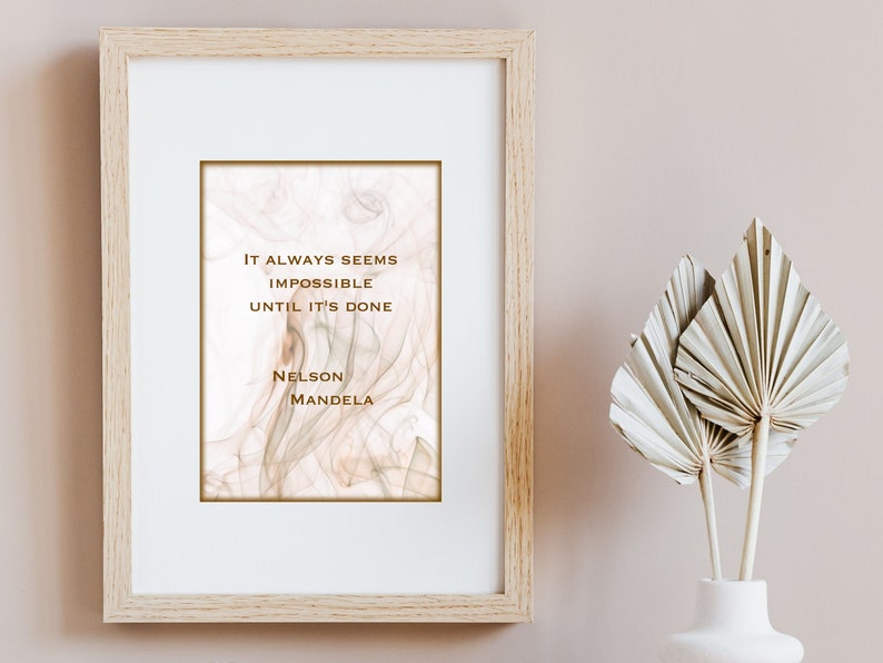 May include: A framed print with a quote by Nelson Mandela: "It always seems impossible until it's done." The background is a soft, abstract design in shades of pink and white.