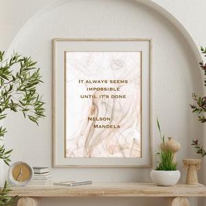 May include: A framed print with a quote by Nelson Mandela on a white background with a subtle brown and pink marbled design. The quote reads "It always seems impossible until it's done."
