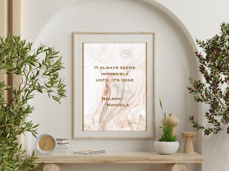 May include: A framed print with a quote by Nelson Mandela on a white background with a subtle brown and pink marbled design. The quote reads "It always seems impossible until it's done."