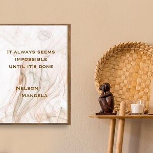 May include: A framed print with a white background and a brown, abstract design. The print features a quote by Nelson Mandela: "It always seems impossible until it's done."