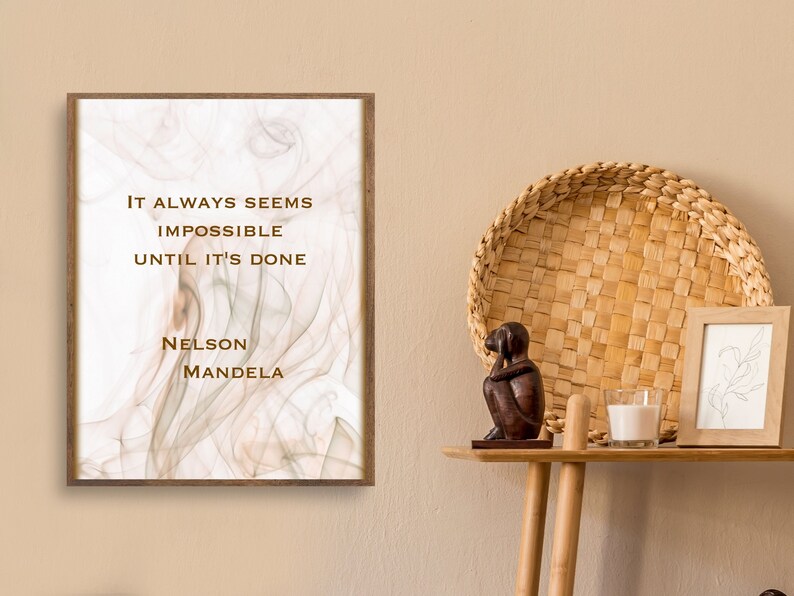 May include: A framed print with a white background and a brown, abstract design. The print features a quote by Nelson Mandela: "It always seems impossible until it's done."
