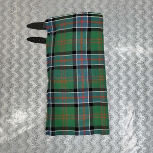 Peut inclure: Un kilt plié à carreaux verts, noirs, bleus et rouges avec deux sangles en cuir noir. Le kilt porte l'inscription "HAND MADE".