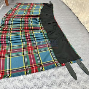 Puede incluir: Un kilt tradicional de tartán con un vibrante patrón de cuadros azules, rojos, verdes y amarillos. El kilt tiene un forro negro y correas de cuero para sujetarlo. El borde con flecos añade un toque clásico a esta prenda.