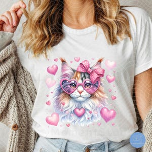 May include: A white t-shirt with a pink and white cat wearing heart-shaped sunglasses and a pink bow. The cat is surrounded by pink hearts.
