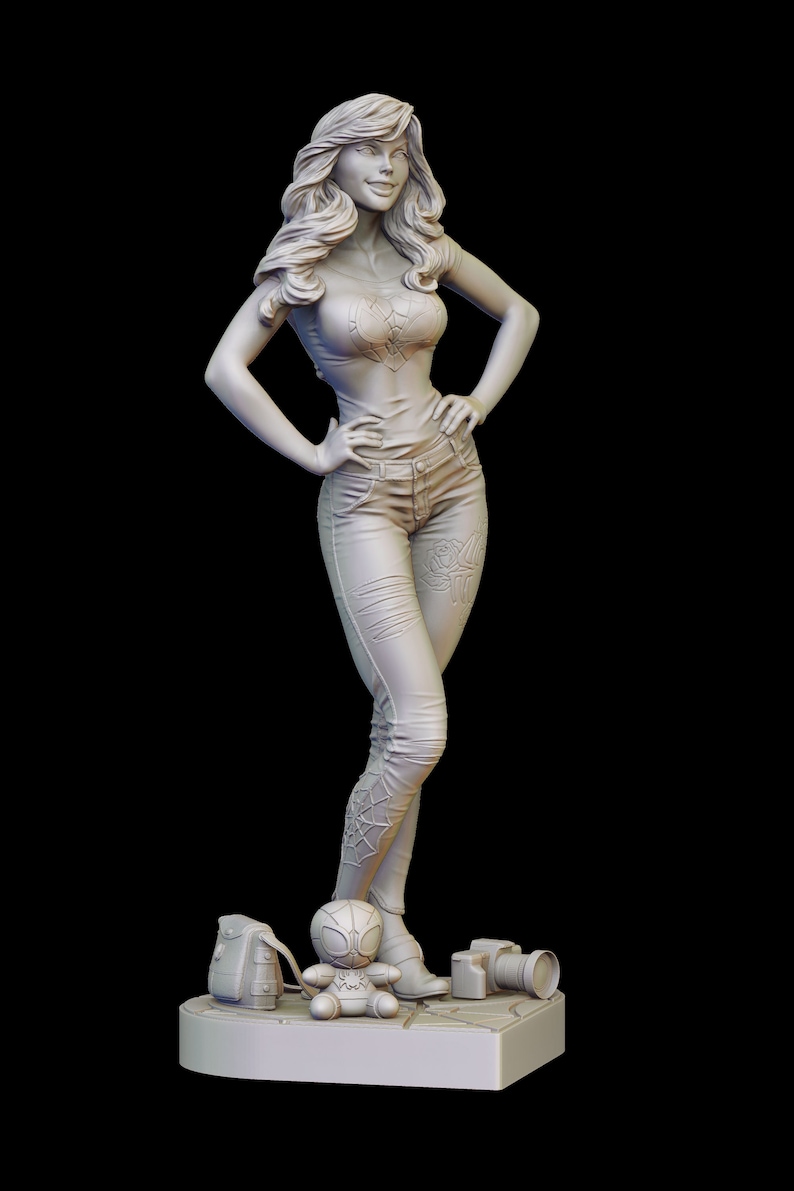 Peut inclure: Une figurine blanche d'une femme aux cheveux longs, portant un t-shirt et un jean. Elle est debout, les mains sur les hanches. Elle tient un appareil photo et une petite figurine d'un homme-araign&eacute;e. La figurine est sur un socle avec une surface textur&eacute;e.