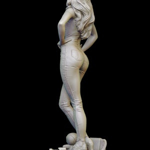 Peut inclure: Une figurine blanche d'une femme portant un jean et une chemise, debout sur une plateforme avec un appareil photo et un sac. La femme est de dos et a les cheveux longs.