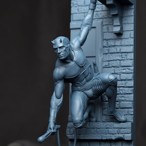 Puede incluir: Una figura gris de un superhéroe en una pose dinámica, aferrado a una pared de ladrillos. La figura lleva una máscara con cuernos y un traje ajustado. Un arma se sostiene en una mano, y un cable se extiende desde ella.