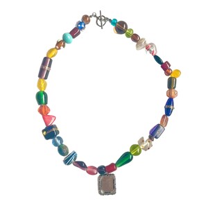 May include: A colourful beaded necklace with a silver clasp and a square pendant. The beads are various shapes and sizes, including round, oval, and rectangular. The colours of the beads include red, orange, yellow, green, blue, purple, and brown.