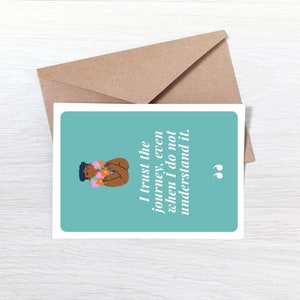 May include: A teal blue card with a quote that reads "I trust the journey, even when I do not understand it." The quote is in white text and is surrounded by a white border. The card features a cartoon illustration of a person with brown skin wearing a flower crown.