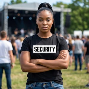 Könnte beinhalten: Ein schwarzes Kurzarm-T-Shirt mit dem Wort SECURITY, das in fetten weißen Großbuchstaben in einem weißen rechteckigen Kasten auf der Brust gedruckt ist. Das Shirt besteht aus einfarbigem schwarzem Stoff mit klassischem Rundhalsausschnitt.
