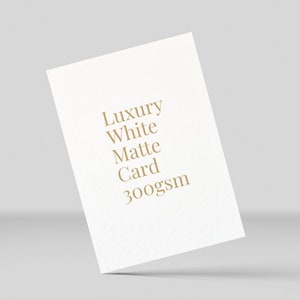 K&ouml;nnte beinhalten: Eine wei&szlig;e Karte mit dem Text "Luxury White Matte Card 300gsm" in Gold gedruckt.