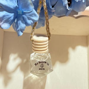 May include: A clear glass bottle with a wooden cap and a gold string hanging from it. The bottle is labeled "My Blossom Co. Green Tea".