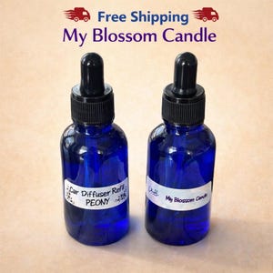 May include: Two cobalt blue glass bottles with black dropper tops. One bottle has a label that reads "Car Diffuser Refill PEONY". The other bottle has a label that reads "My Blossom Candle".