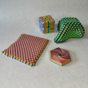 Könnte beinhalten: Eine Sammlung farbenfroher, geometrischer 3D-gedruckter Objekte. Dazu gehören ein Würfel, eine gebogene Form, ein flaches Quadrat und ein mehrschichtiges Sechseck. Die Objekte weisen einen Farbverlauf auf, darunter Rosa, Blau, Grün und Gelb.