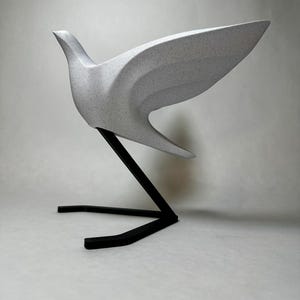 Könnte beinhalten: Eine weiße Keramik-Taubenskulptur mit geometrischem Design, auf einem schwarzen Metallständer.