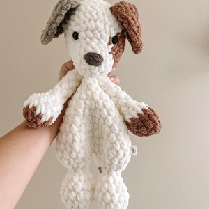 Pu&ograve; includere: Peluche di cane in crochet bianco con dettagli marroni e grigi. Il giocattolo ha un viso cucito con occhi neri e un naso marrone.