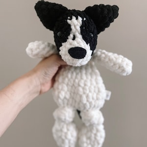 Pu&ograve; includere: Un giocattolo di peluche a forma di cane in crochet bianco e nero con occhi neri e naso nero. Il giocattolo ha una coda lunga e quattro zampe.