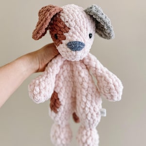 Pu&ograve; includere: Un giocattolo per cani in crochet rosa con macchie marroni e grigie. Il cane ha un naso e occhi cuciti.