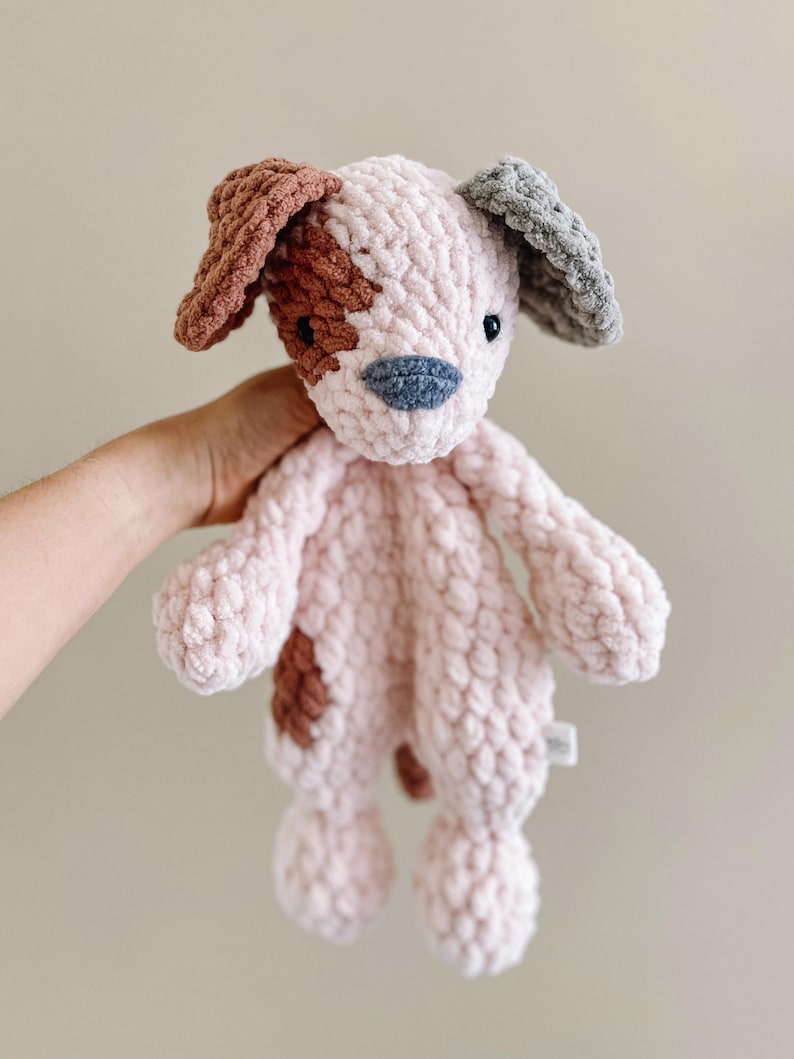 Pu&ograve; includere: Un giocattolo per cani in crochet rosa con macchie marroni e grigie. Il cane ha un naso e occhi cuciti.